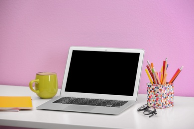 Photo of Modern laptop on table against color wall. Mock up with space for text