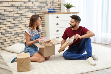 Photo of Young couple opening parcels on floor at home