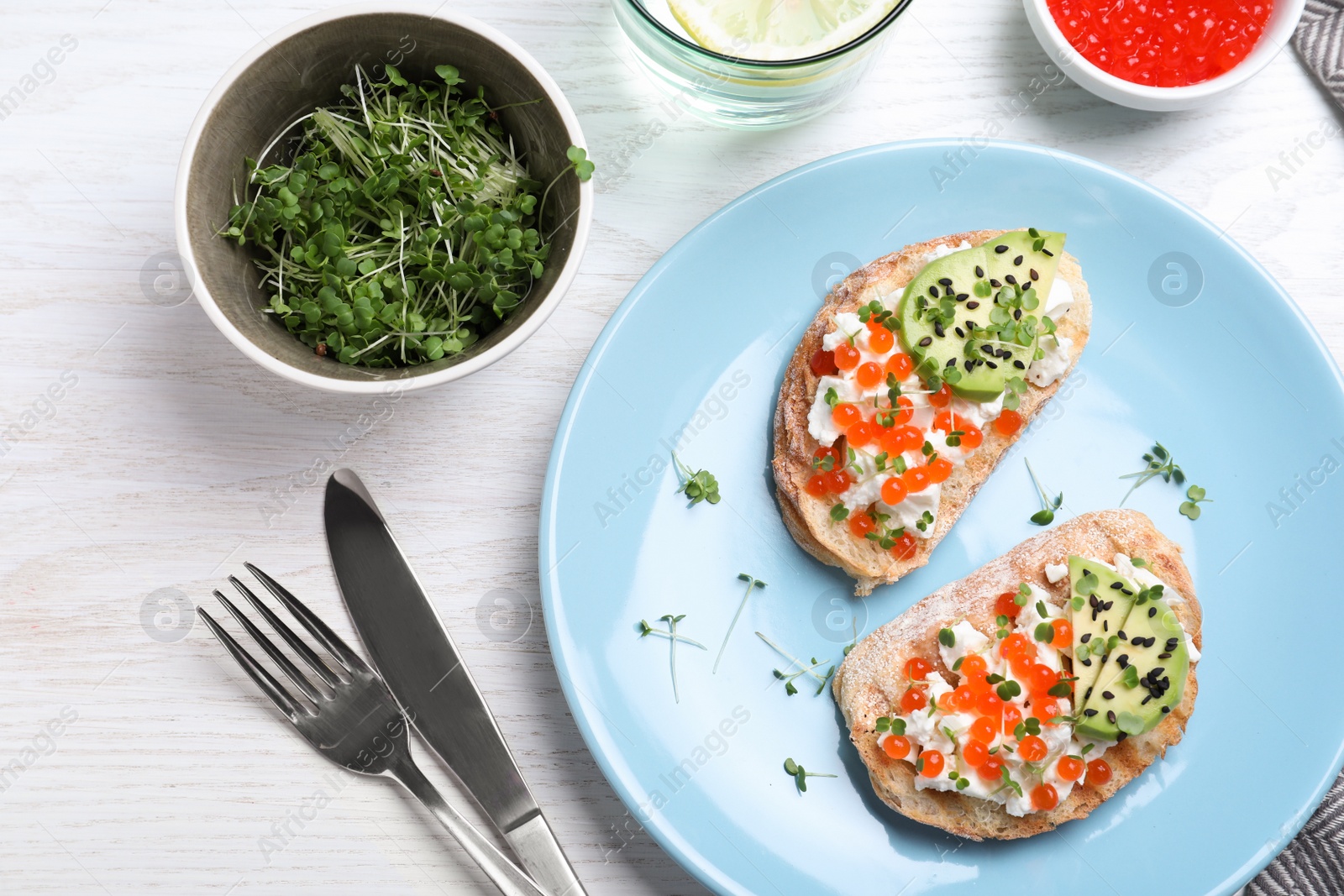 Photo of Delicious sandwiches with caviar, cheese, avocado and microgreens on white wooden table, flat lay