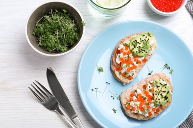 Photo of Delicious sandwiches with caviar, cheese, avocado and microgreens on white wooden table, flat lay
