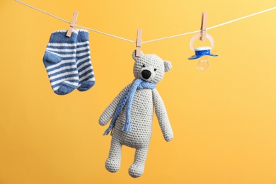 Photo of Small socks, pacifier and toy bear hanging on washing line against color background. Baby accessories