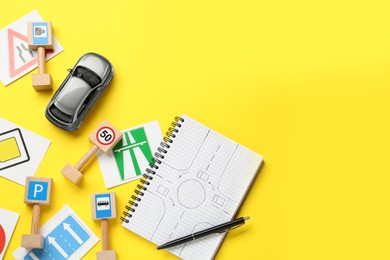 Many different road signs, notebook and toy car on yellow background, flat lay with space for text. Driving school