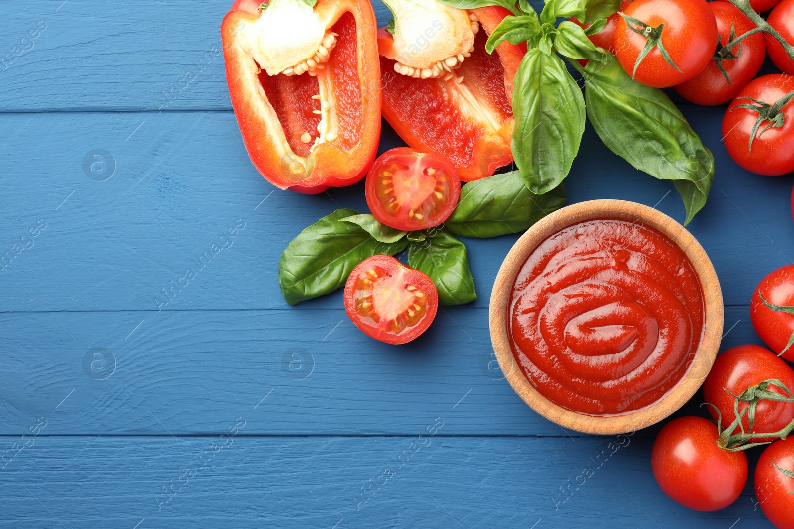 Photo of Bowl of tasty ketchup and ingredients on blue wooden table, flat lay. Space for text