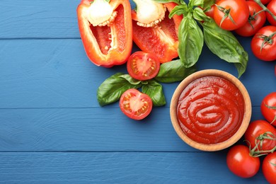 Photo of Bowl of tasty ketchup and ingredients on blue wooden table, flat lay. Space for text