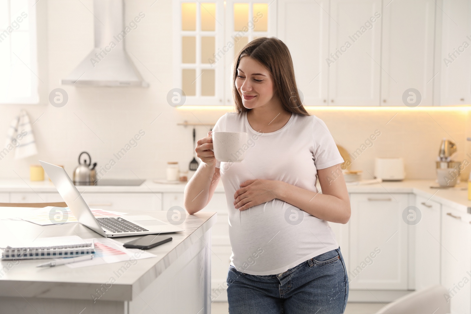 Photo of Pregnant woman working in kitchen at home. Maternity leave