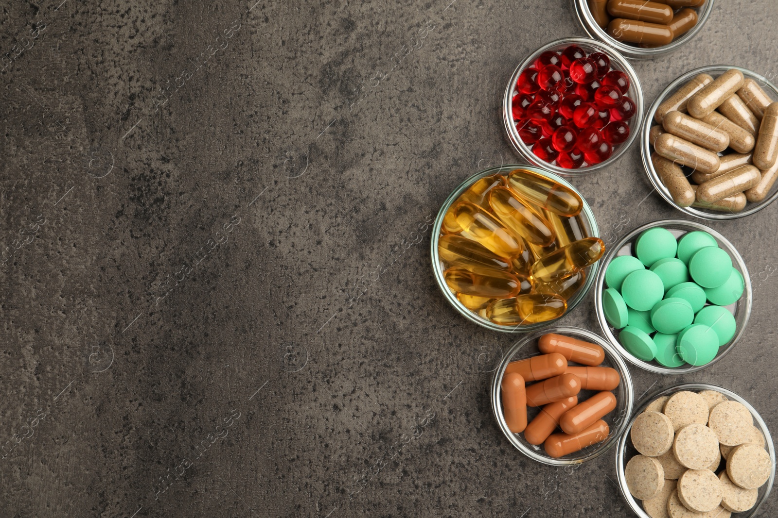 Photo of Different dietary supplements in glass bowls on grey table, flat lay. Space for text