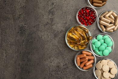 Different dietary supplements in glass bowls on grey table, flat lay. Space for text