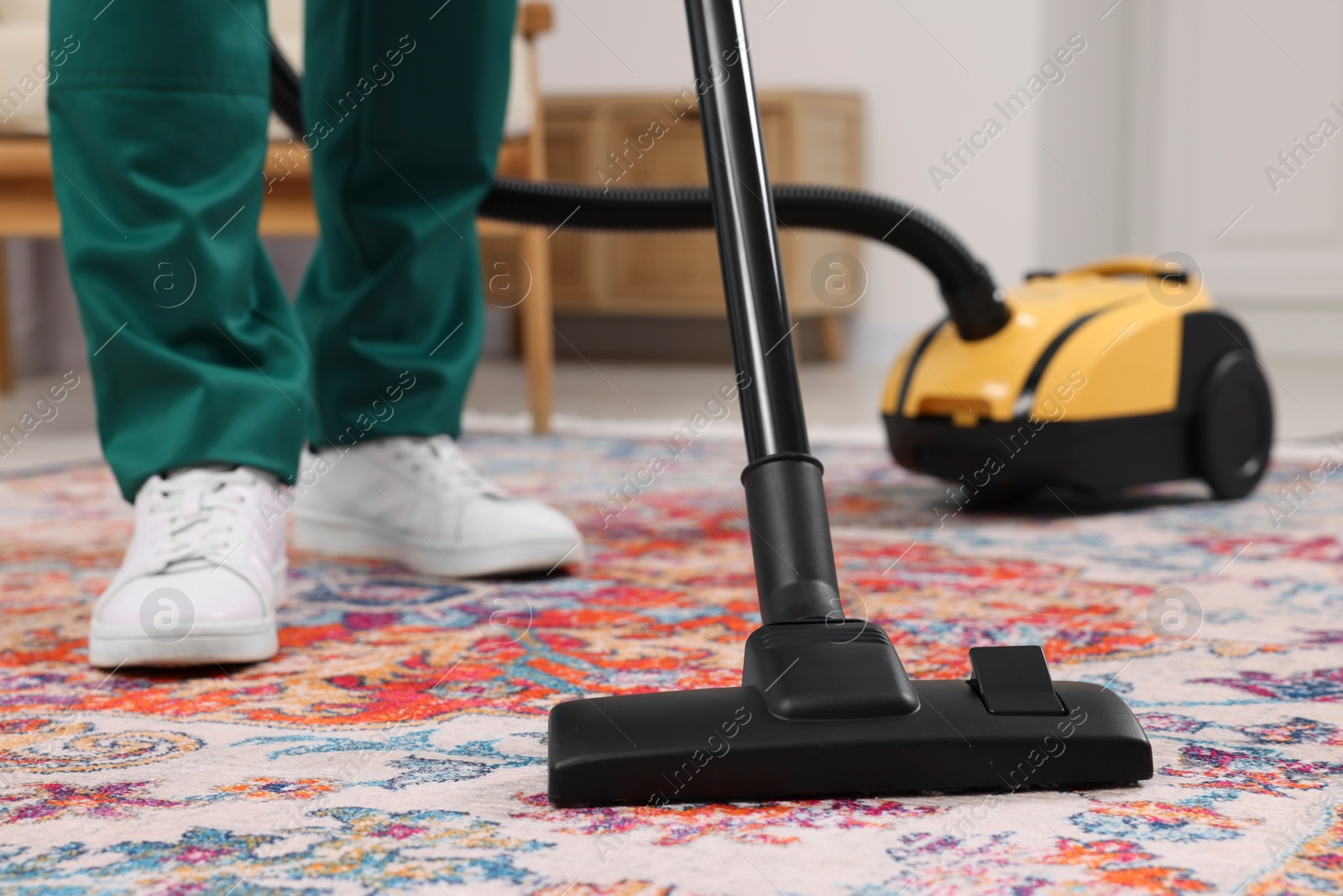 Photo of Dry cleaner's employee hoovering carpet with vacuum cleaner indoors, closeup