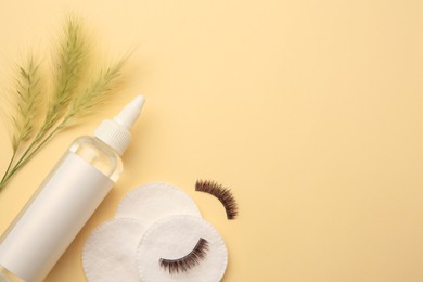 Bottle of makeup remover, cotton pads, false eyelashes and spikelets on yellow background, flat lay. Space for text