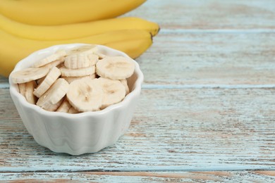Photo of Bowl with cut bananas near whole fruits on light wooden table, closeup. Space for text