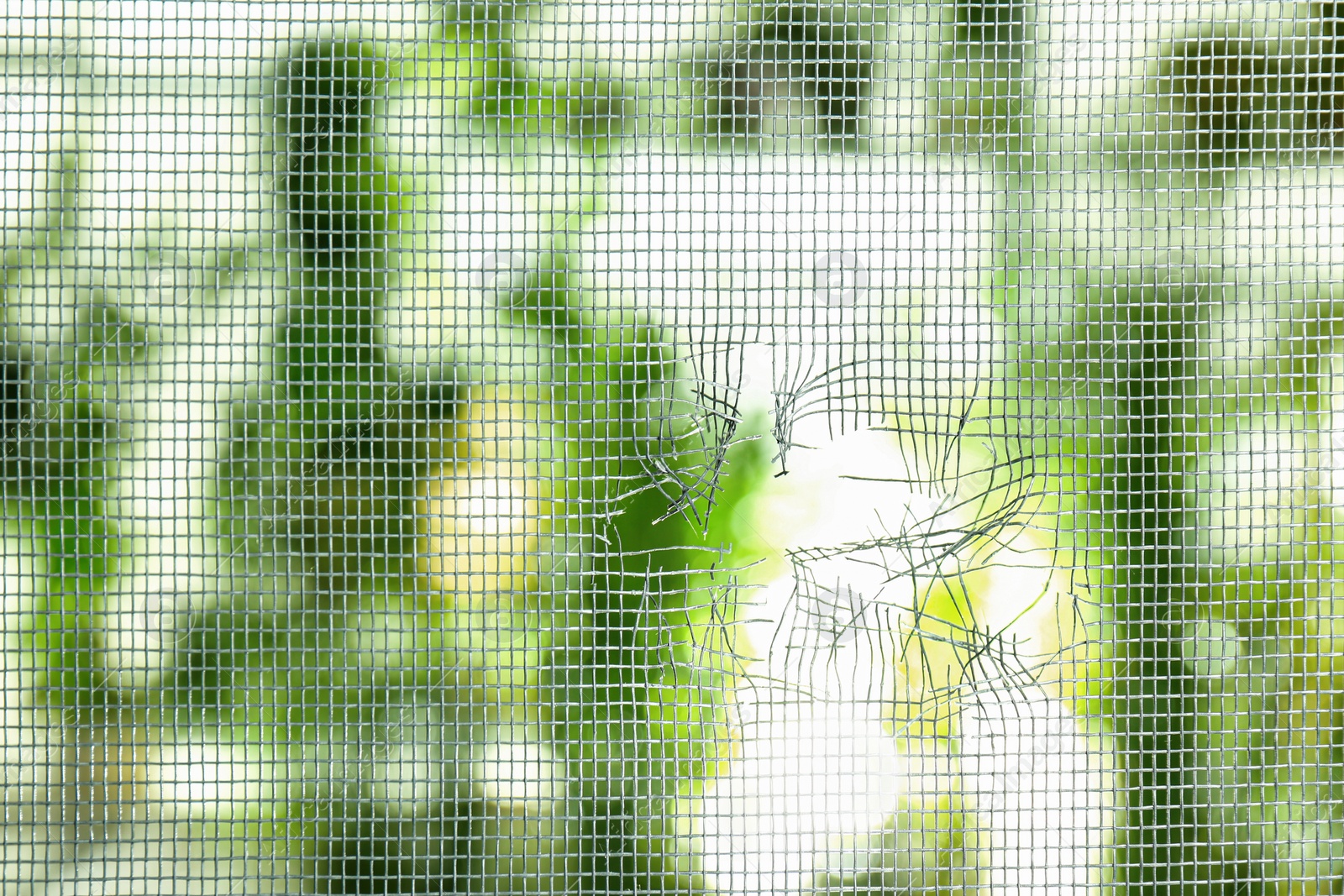 Photo of Torn window screen against blurred background, closeup