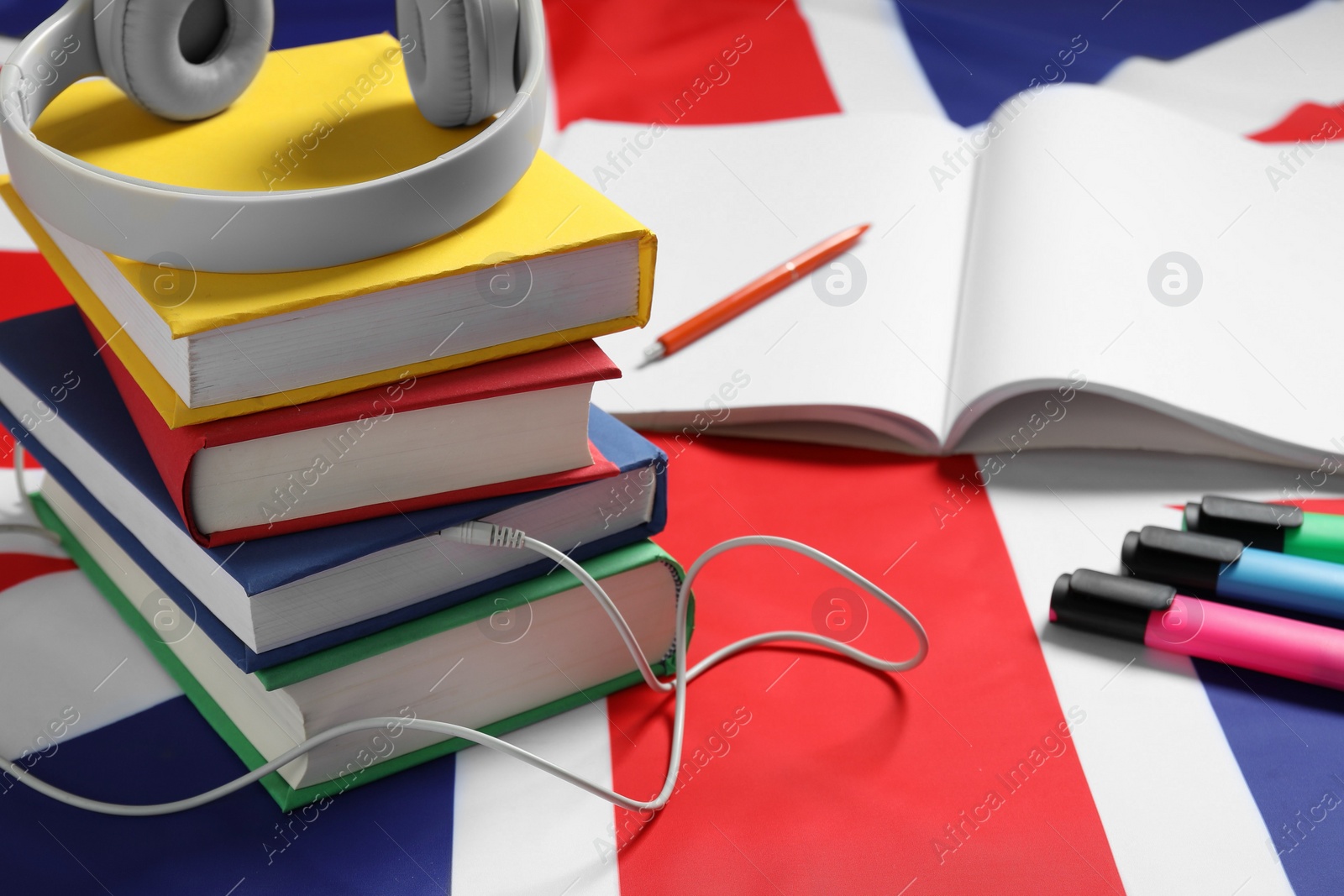 Photo of Learning foreign language. Different books, headphones and stationery on flag of United Kingdom, space for text