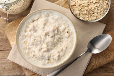 Photo of Tasty boiled oatmeal in bowl, flakes and spoon on wooden table, flat lay