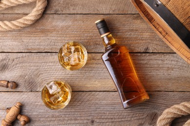 Photo of Whiskey with ice cubes in glasses, bottle and barrel on wooden table, flat lay