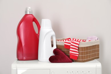 Photo of Baby clothes in wicker basket and laundry detergents on washing machine near light wall, space for text