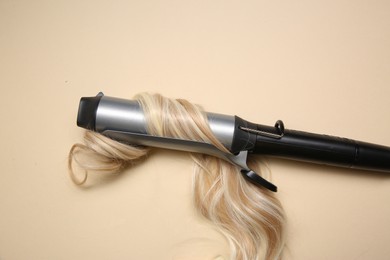 Curling iron with blonde hair lock on beige background
