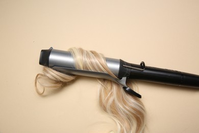 Photo of Curling iron with blonde hair lock on beige background