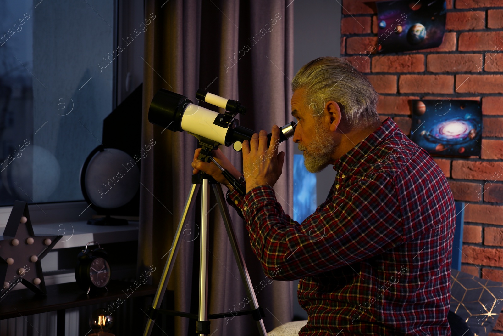 Photo of Senior man looking at stars through telescope in room