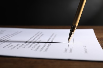 Photo of Signing document with pen on wooden table, closeup