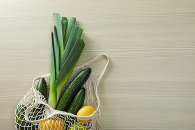 Net bag with vegetables and fruits on wooden table, top view. Space for text