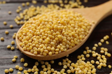 Spoon with millet groats on wooden table, closeup