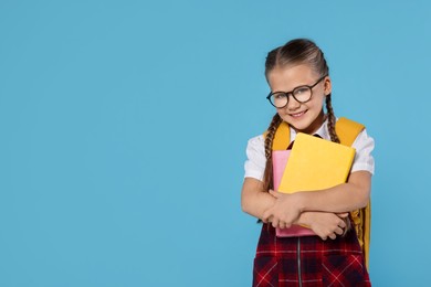 Photo of Happy schoolgirl in glasses with backpack and books on light blue background, space for text