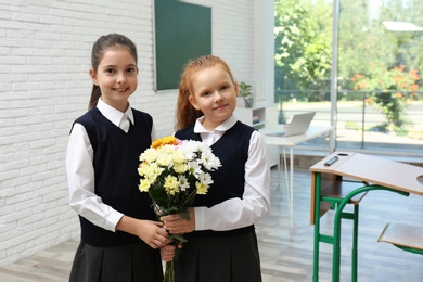 Happy schoolgirls with bouquet in classroom. Teacher's day