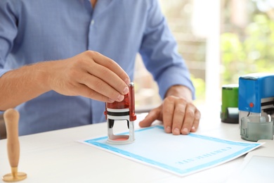 Photo of Male notary stamping document at table in office, closeup