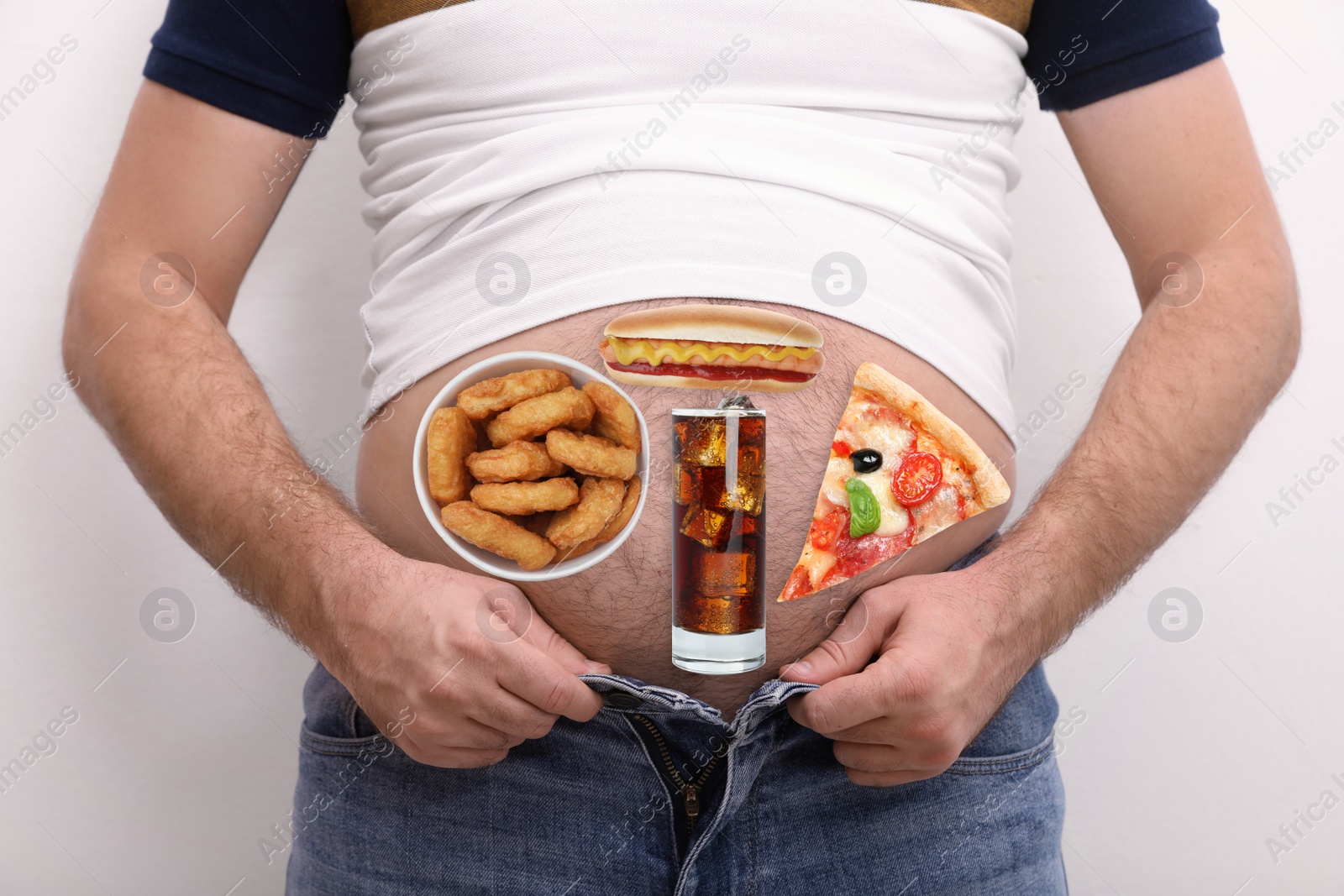 Image of Man wearing tight t-shirt and jeans with images of different unhealthy food on his belly against white background