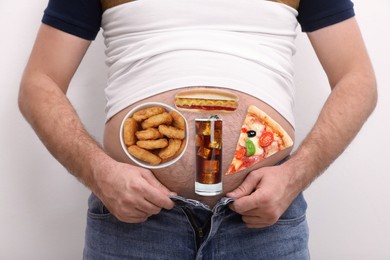 Image of Man wearing tight t-shirt and jeans with images of different unhealthy food on his belly against white background