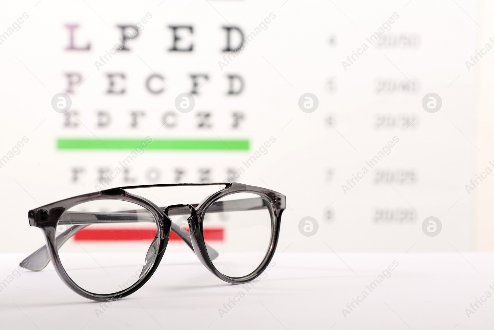 Glasses with corrective lenses on table against eye chart Photo of Glasses with corrective lenses on table against eye chart