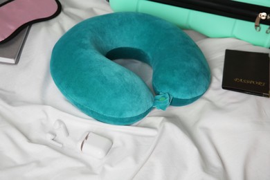 Photo of Turquoise travel pillow, suitcase, passport, sleep mask and earphones on bed