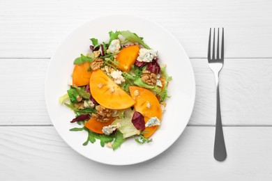 Photo of Delicious persimmon salad and fork on white wooden table, flat lay