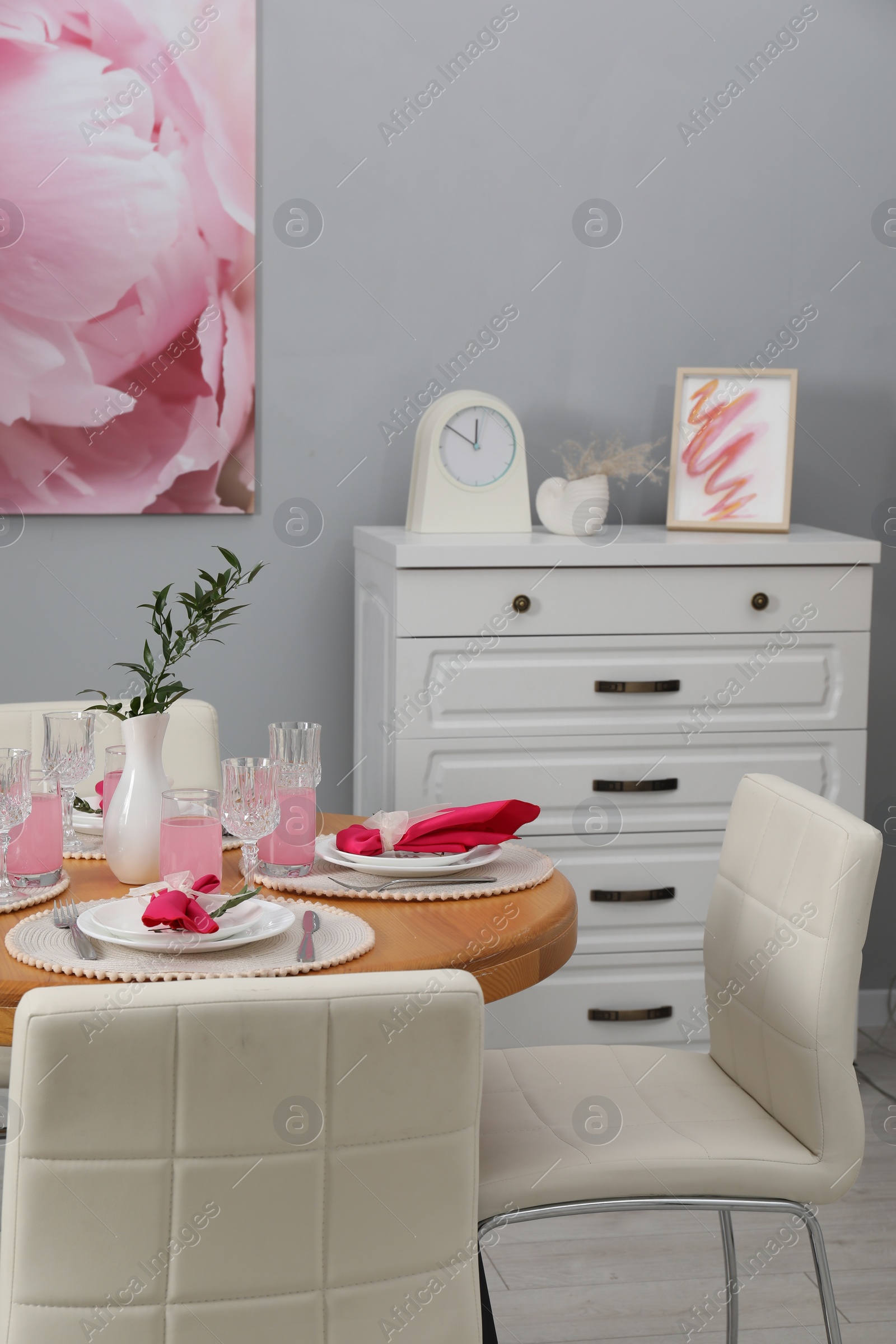 Photo of Color accent table setting. Glasses, plates, vase with green branch and pink napkins in dining room