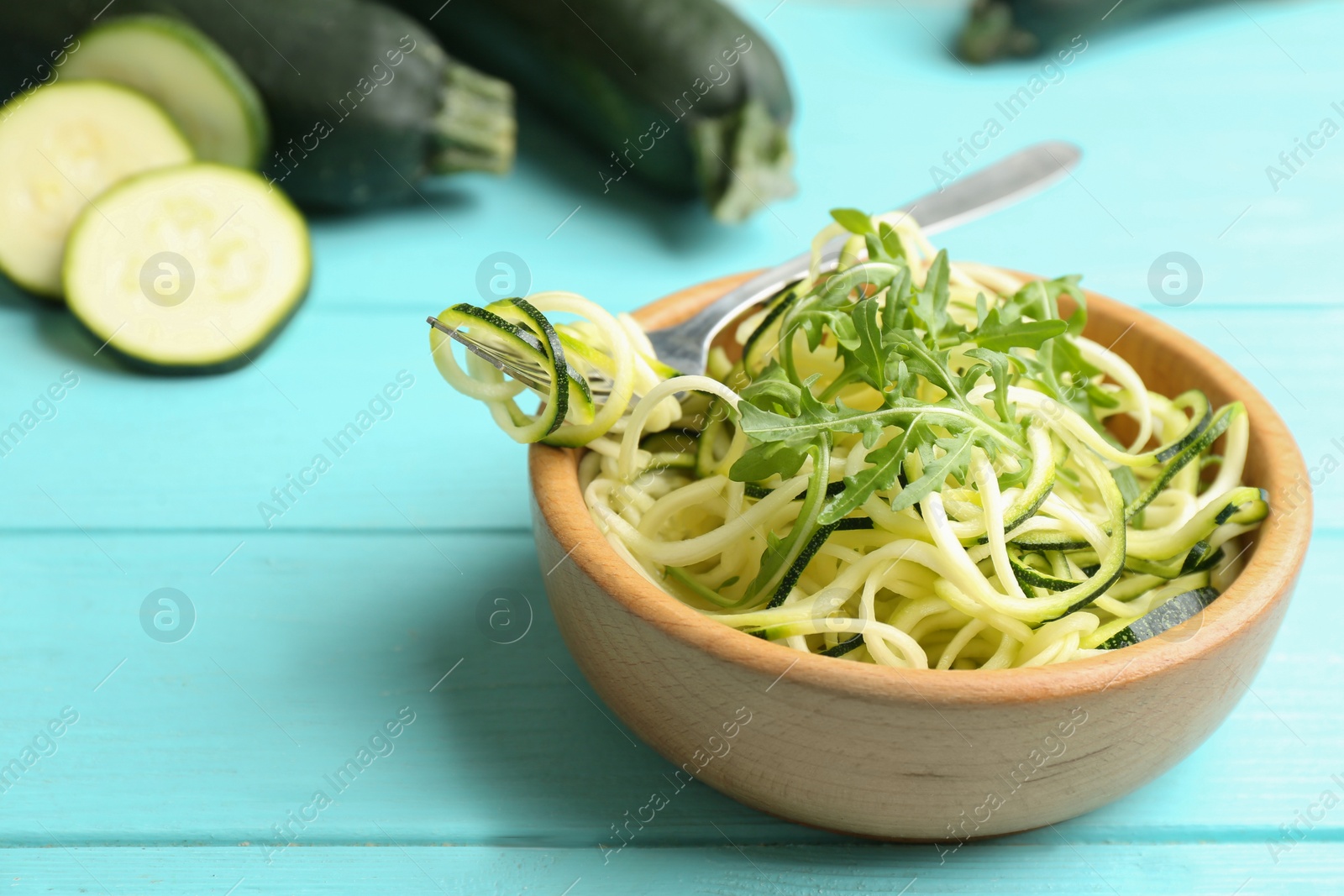 Photo of Delicious zucchini pasta with arugula in bowl on light blue wooden table