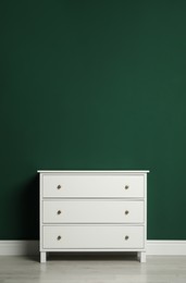 Photo of Modern white chest of drawers near green wall indoors