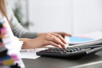 Photo of Office employee working with calculator and documents at table, closeup