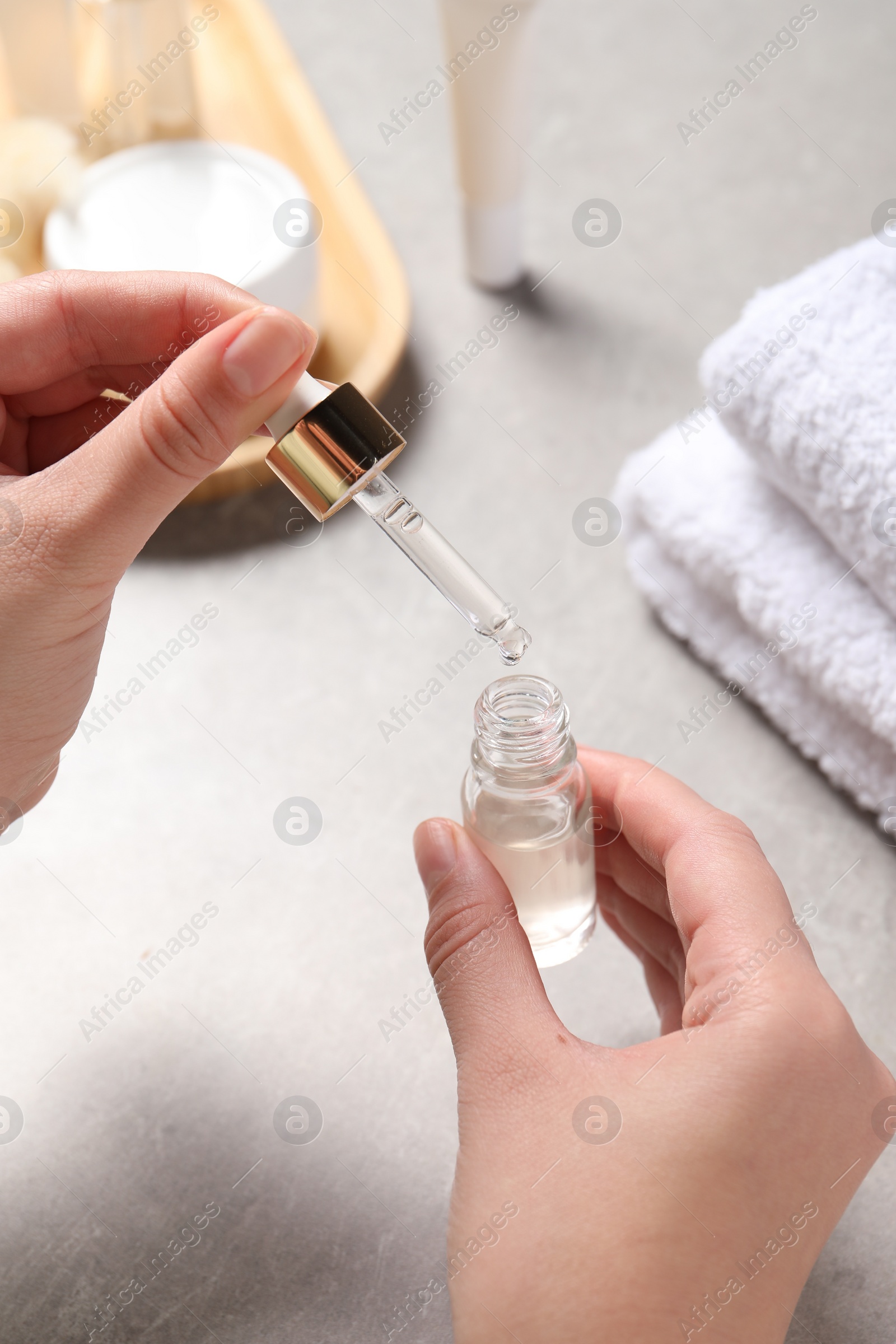 Photo of Woman with bottle of cosmetic serum and pipette at light table, closeup