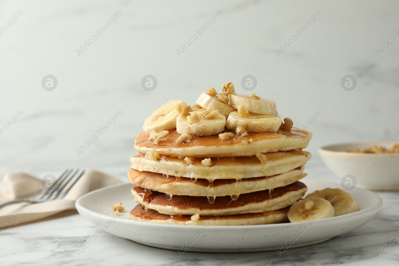 Photo of Delicious pancakes with bananas, walnuts and honey on white marble table, closeup