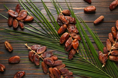 Tasty sweet dried dates and palm leaf on wooden table, flat lay