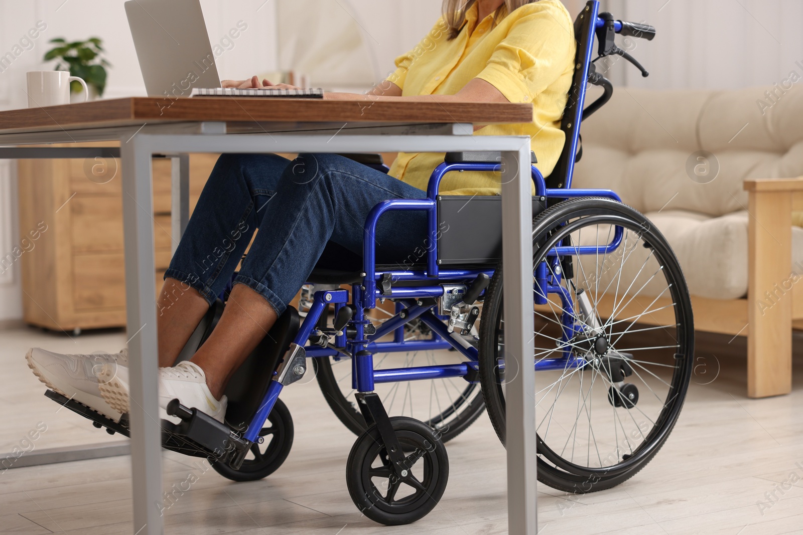 Photo of Woman in wheelchair using laptop at table in home office, closeup