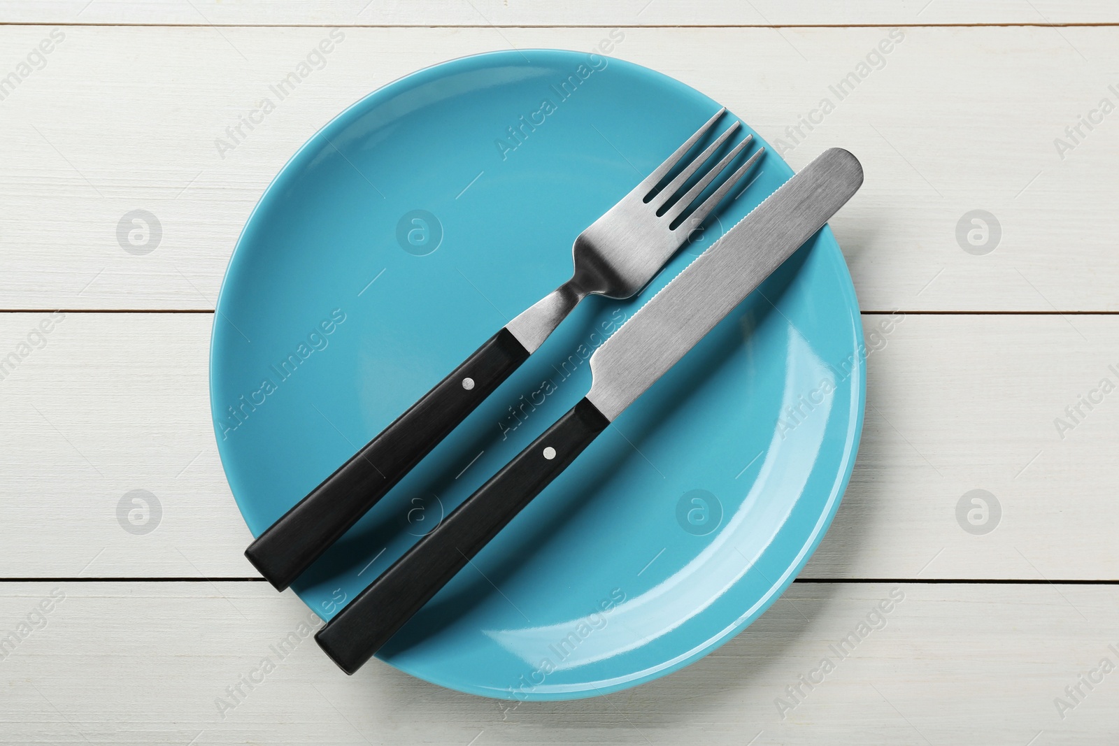 Photo of Light blue ceramic plate with cutlery on white wooden table, top view