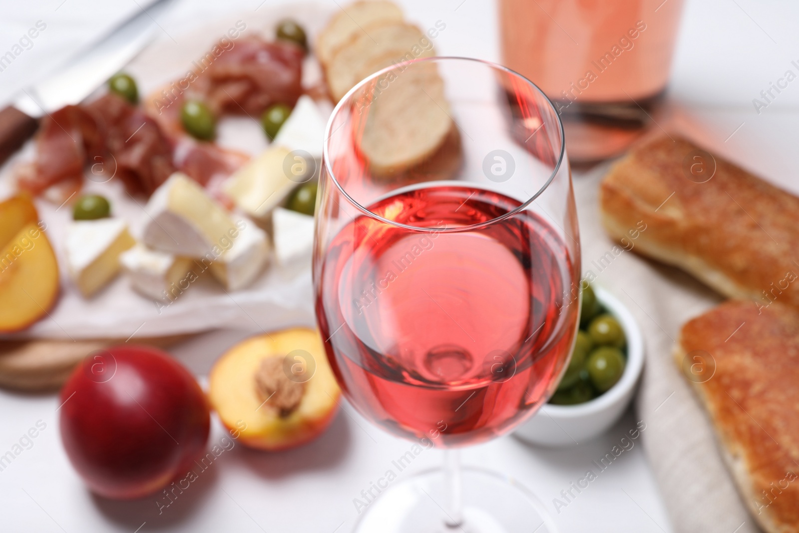 Photo of Glass of delicious rose wine and snacks on white table, closeup