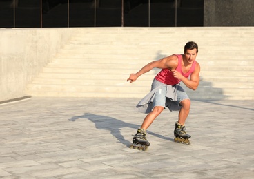 Photo of Handsome young man roller skating on city street, space for text