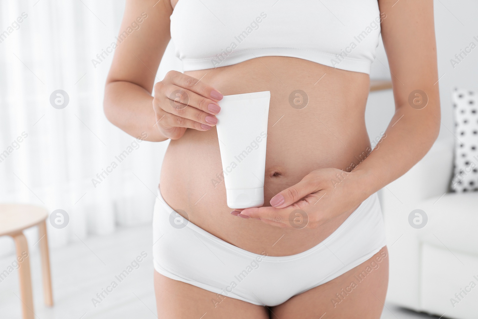 Photo of Pregnant woman holding body cream at home, closeup