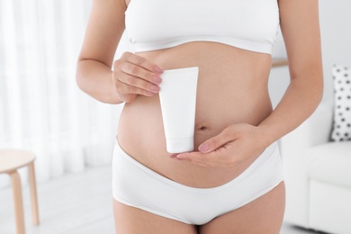 Pregnant woman holding body cream at home, closeup