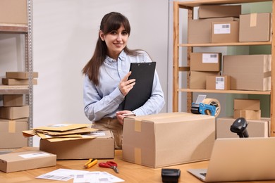 Parcel packing. Post office worker with clipboard at wooden table indoors