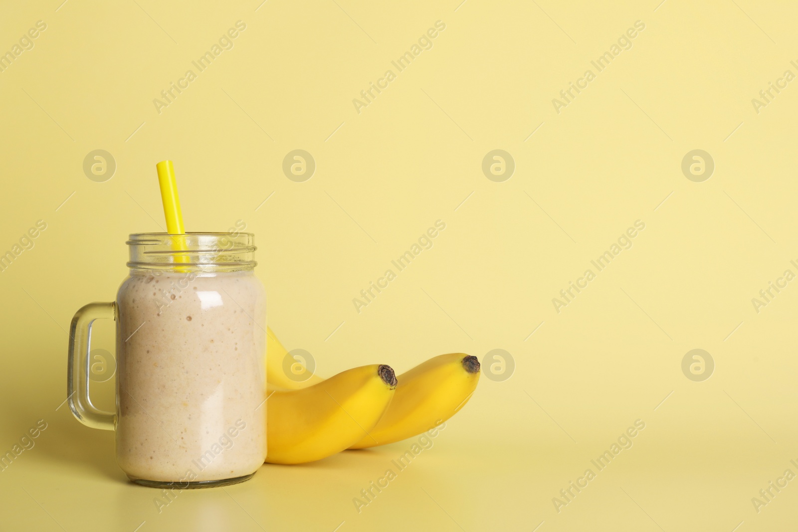 Photo of Mason jar with tasty smoothie and bananas on beige background. Space for text