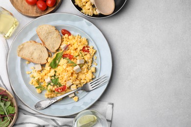 Delicious scrambled eggs with tofu and slices of baguettes served on light grey table, flat lay. Space for text