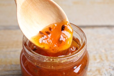 Spoon with sea buckthorn jam in jar on table, closeup